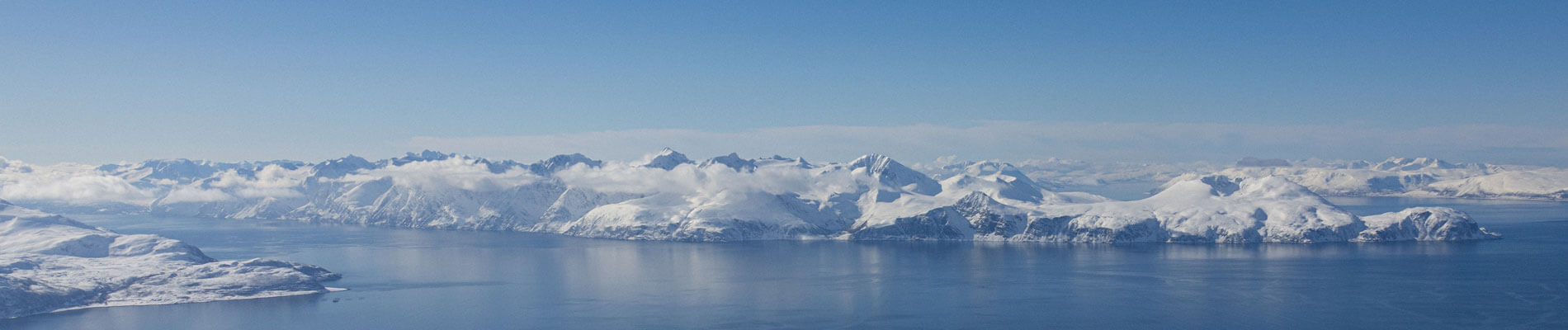 Photographie panoramique de montagne enneigées, entouré de fjords, dans les Alpes de Lyngen, en Norvège.